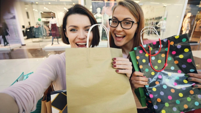 Two happy women holding shopping bags in a mall.